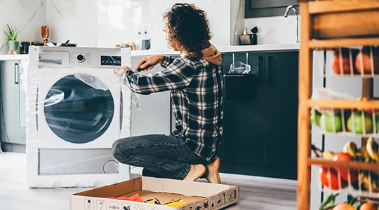 Person squatting to unrap a new washing machine for installation.